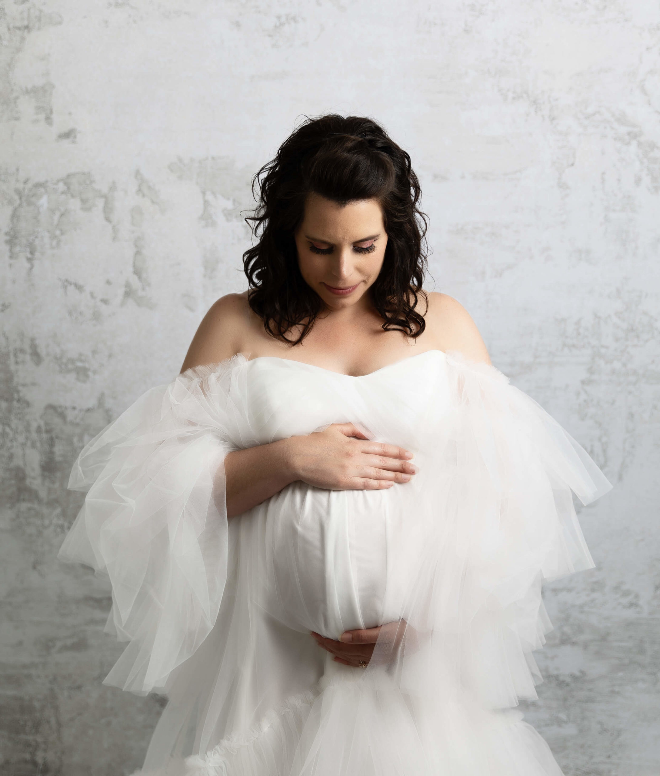 Maternity photo of a girl looking at her belly in a white dress