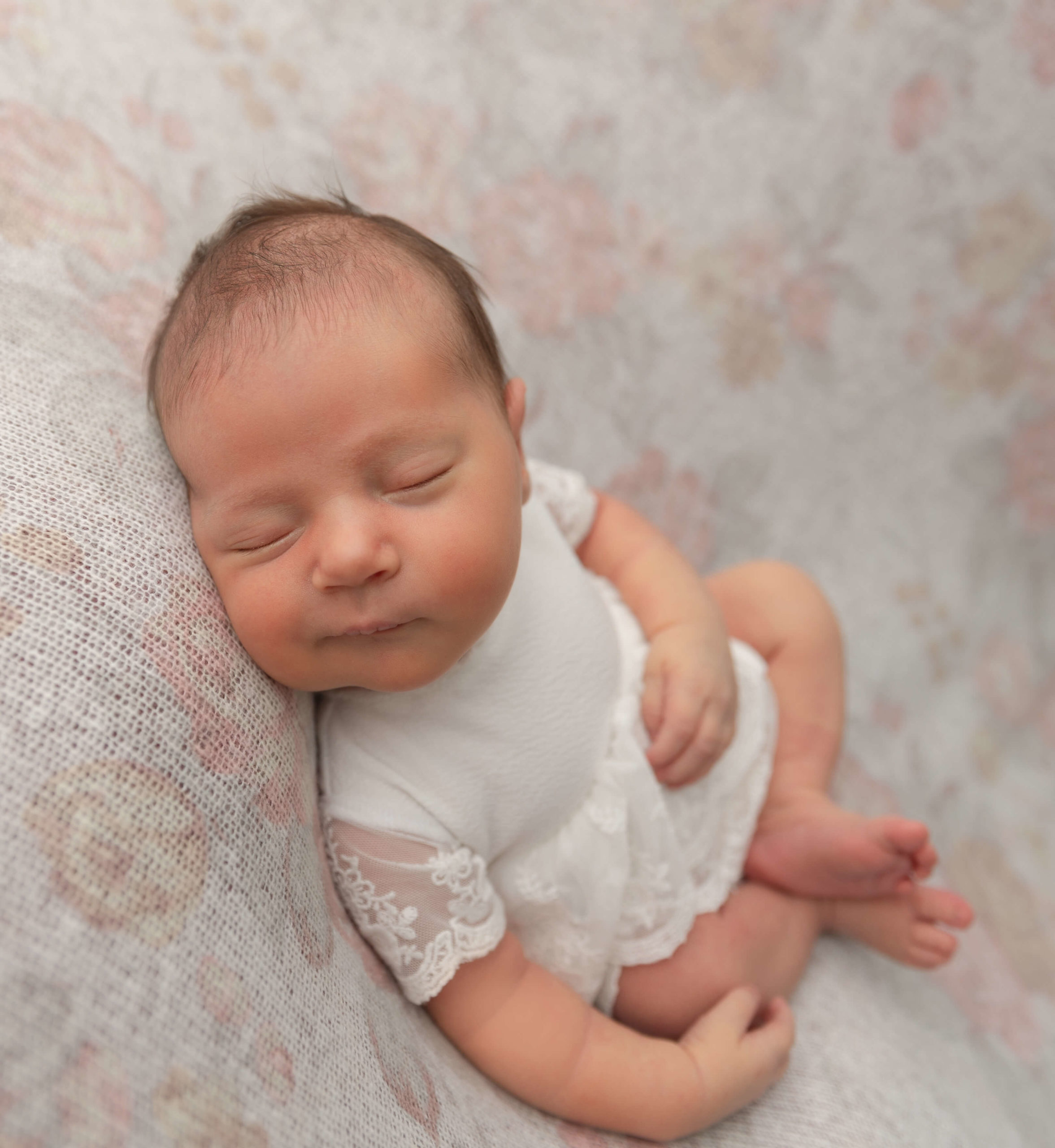 Picture of a newborn baby girl laying on a flower backdrop smiling