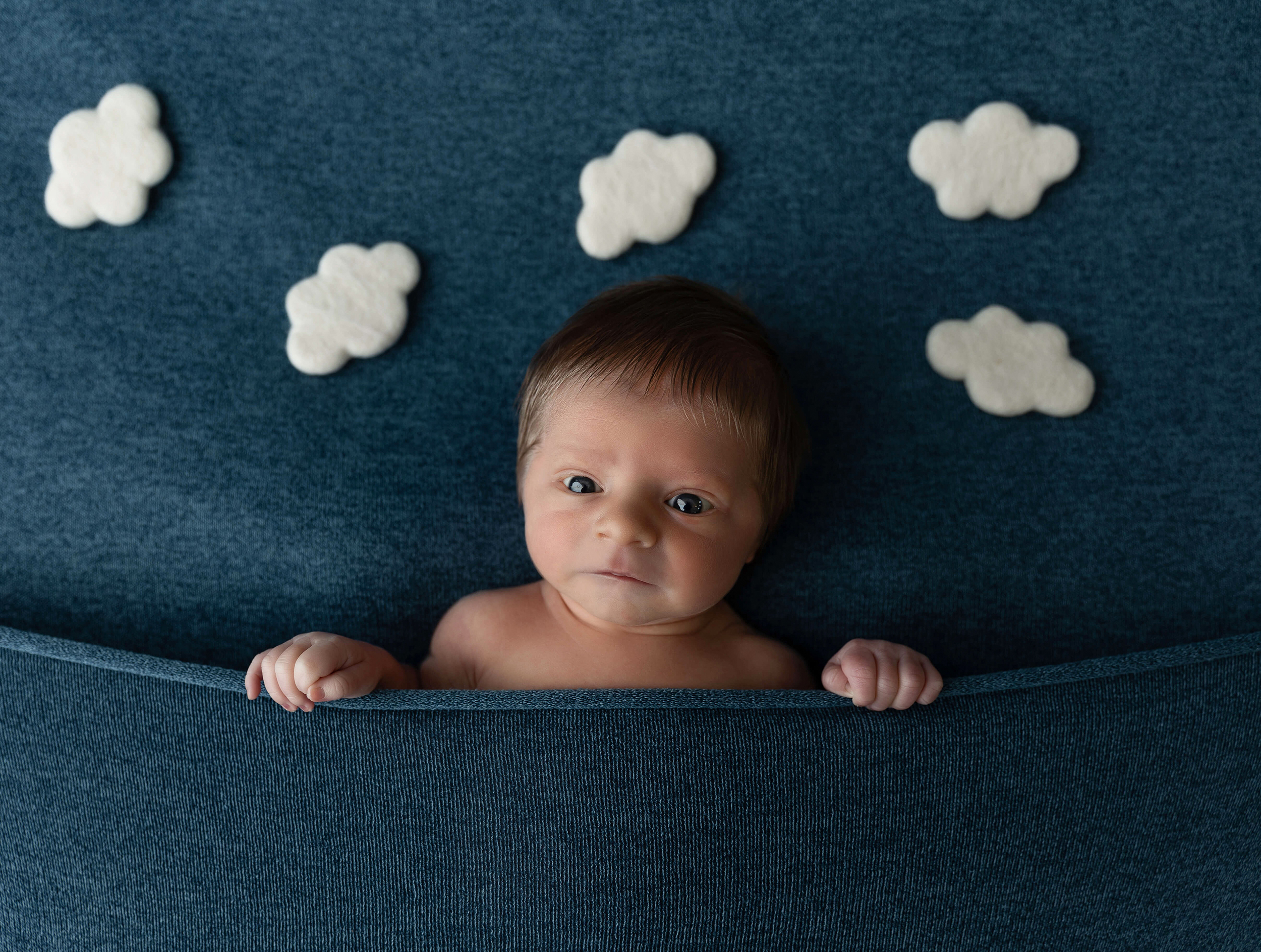 Newborn baby laying on a blue blanket with clouds