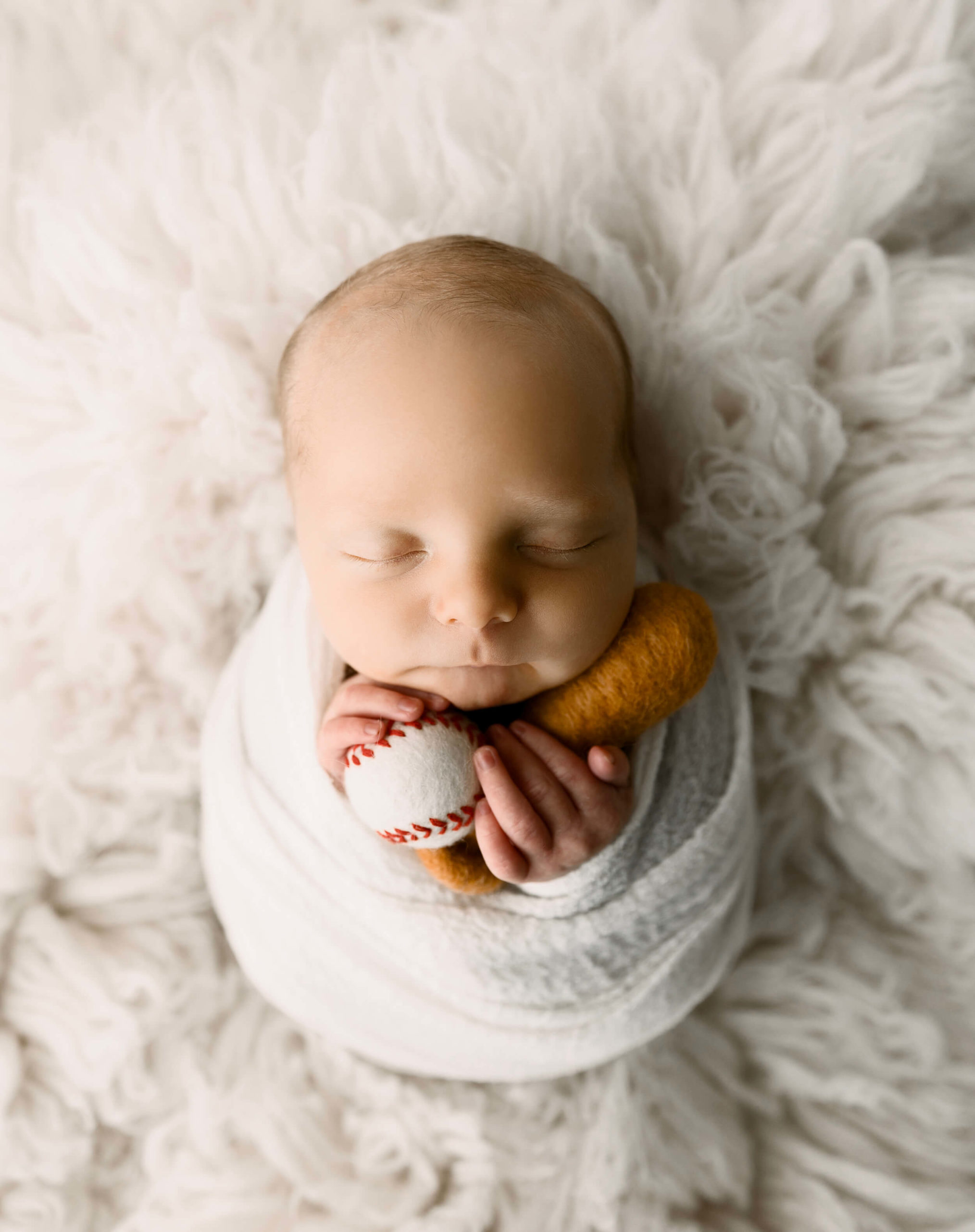 Newborn photo of a baby boy wrapped holding a bat and ball