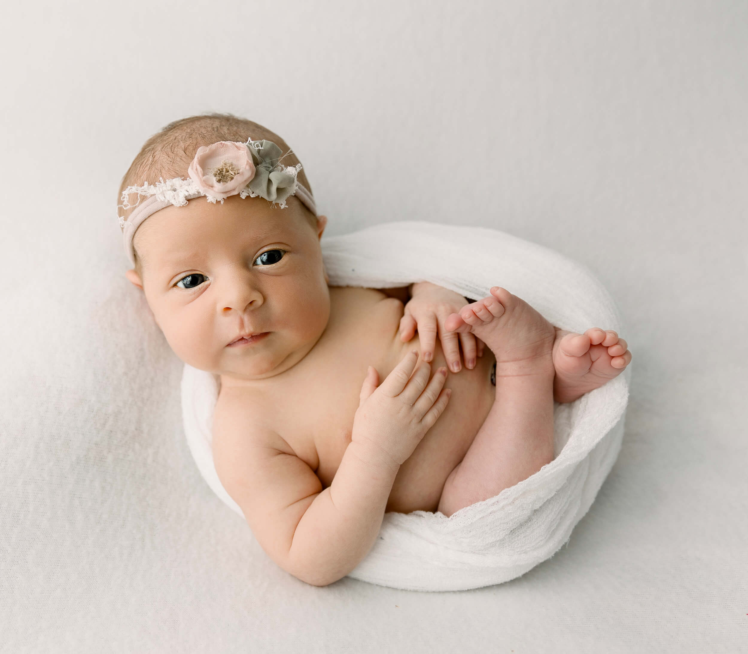A newborn baby girl in an egg wrap pose in a photography studio