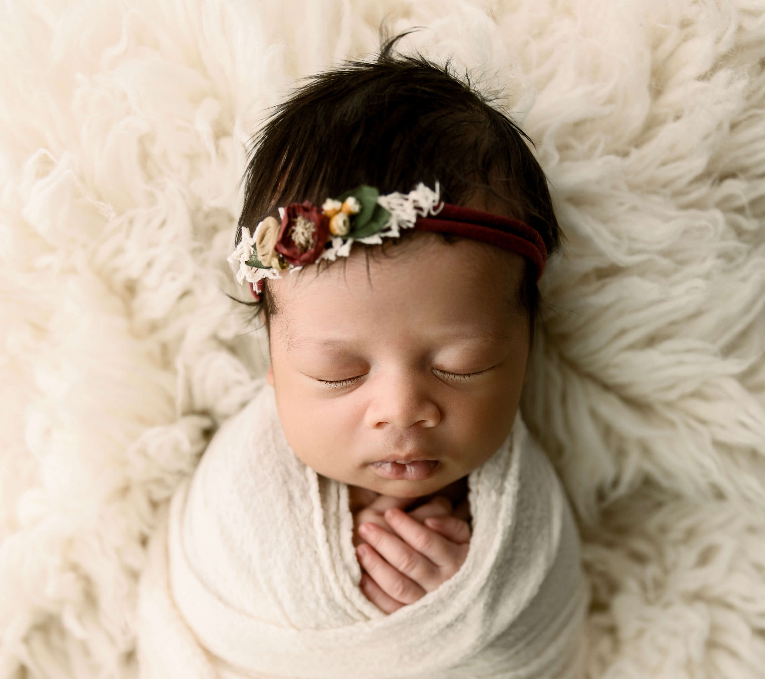 Newborn baby girl with a beautiful headband laying on flokati fur