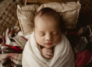 Newborn photo of a baby boy wrapped and laying on a plaid blanket