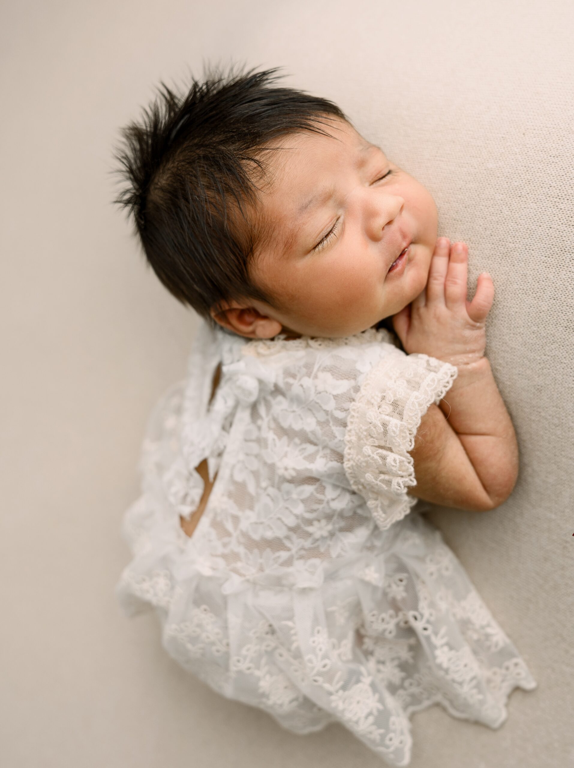 A newborn baby sleeps in her white lace dress on her belly after meeting nanny erie pa