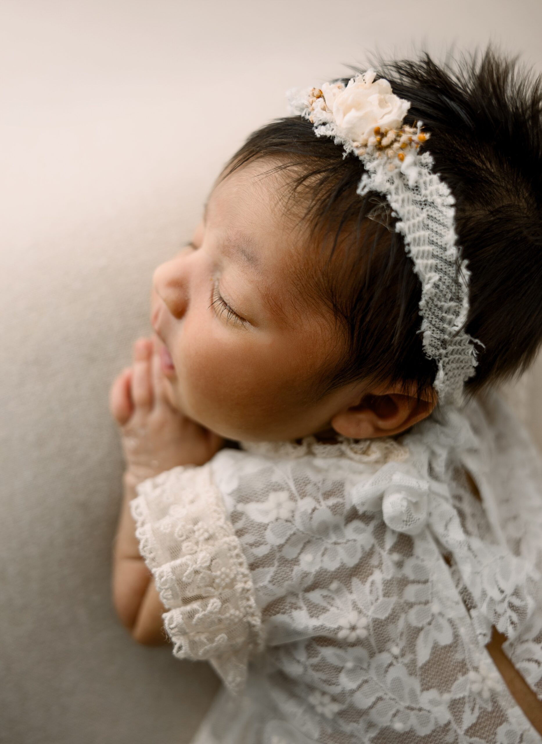 Details of a newborn baby girl sleeping in a white lace dress on a bed in a studio after finding a nanny erie pa