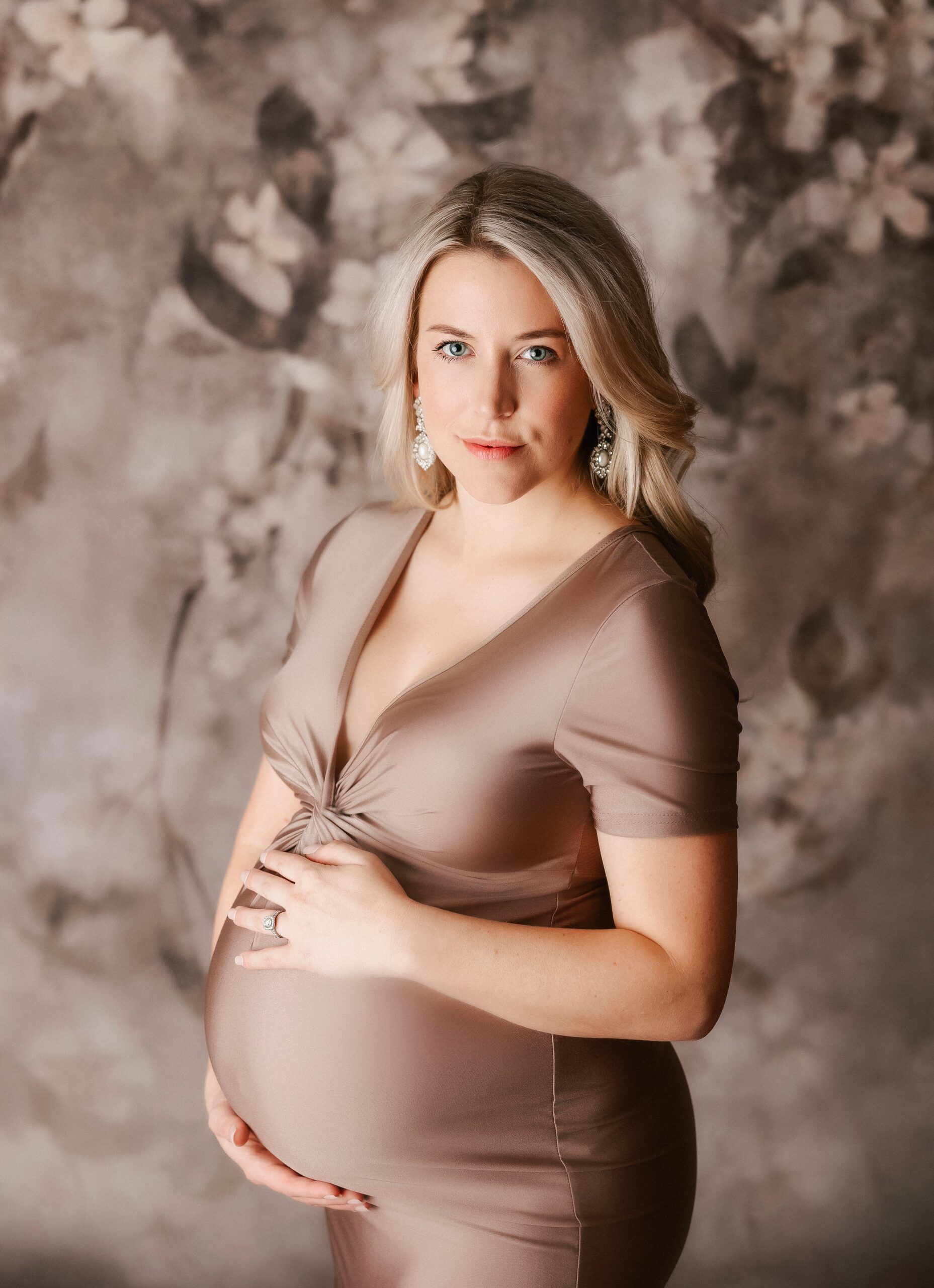 A mother to be in a brown maternity gown stands in a studio while holding the bump after meeting northwest doulas