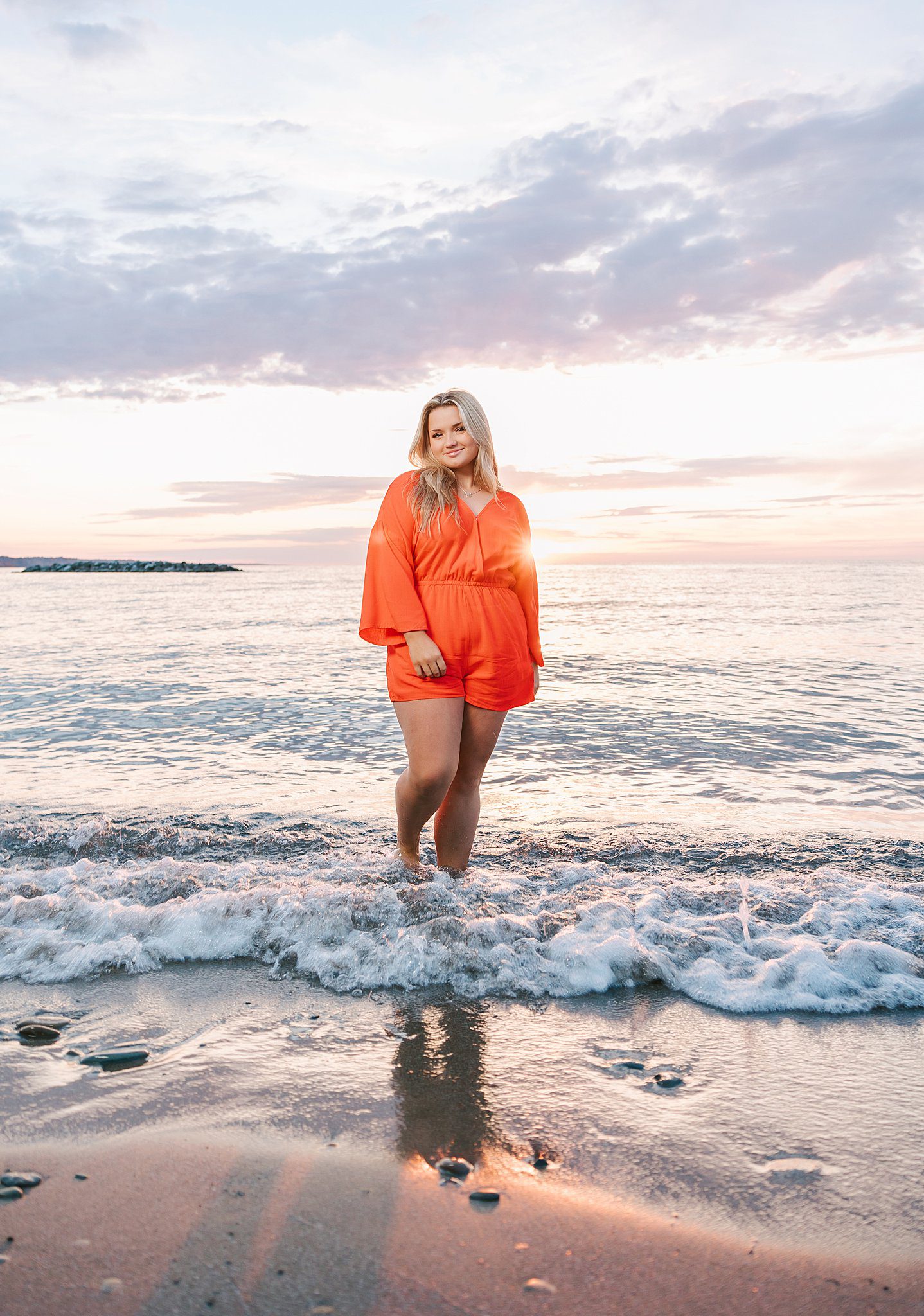A blonde woman in a red romper walks in the water on the beach at sunset after visiting hair salons erie pa