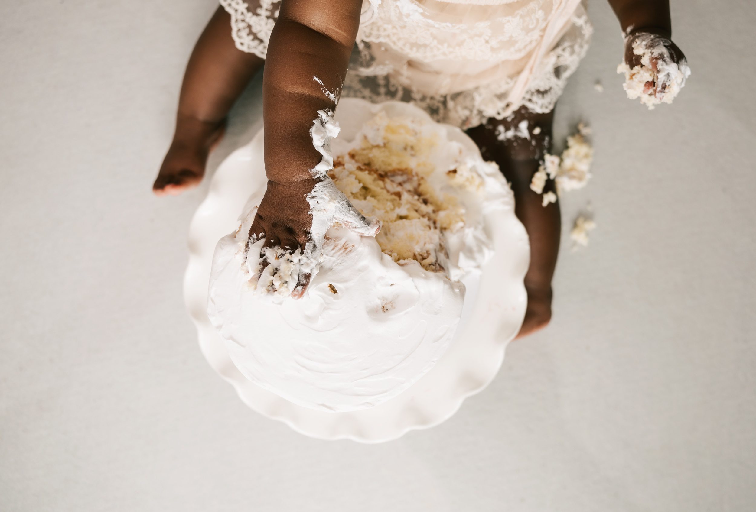 A look down at a toddler girl smashing a cake in a white lace dress before visiting kid friendly restaurants erie pa