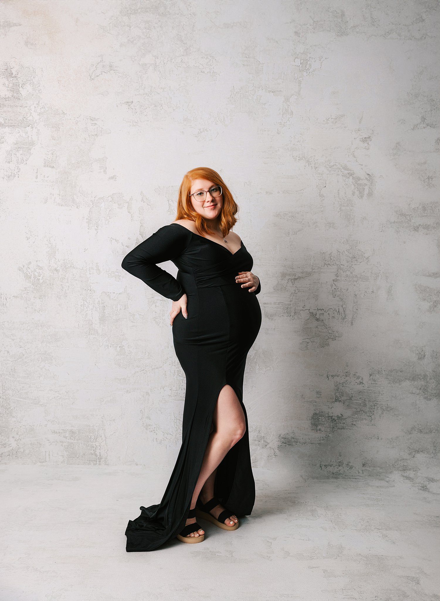 A mother to be in a long black maternity gown smiles while standing in a studio after visiting an obgyn erie pa