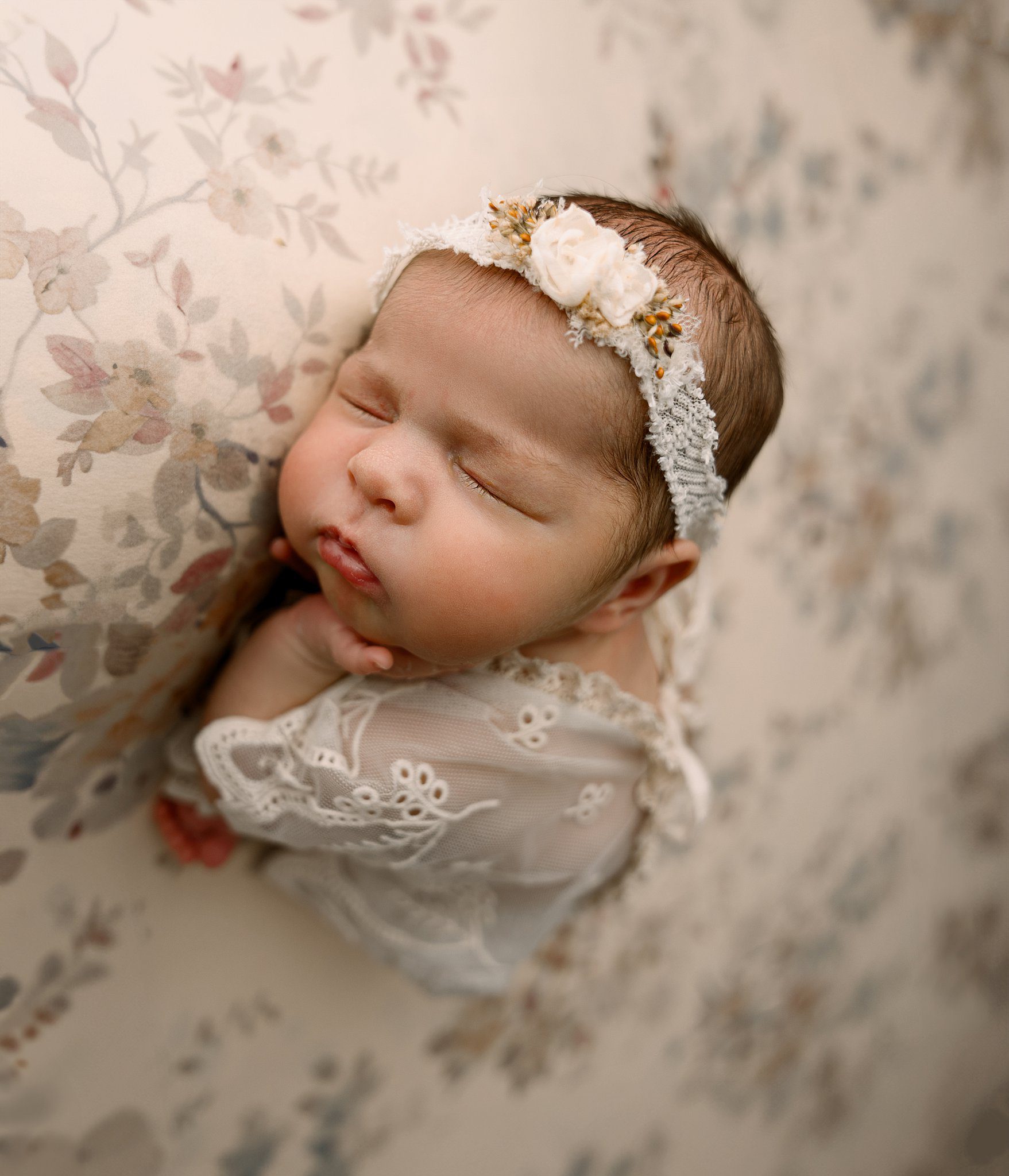 Details of a sleeping newborn baby face in a lace dress with floral headband before some parenting classes erie pa