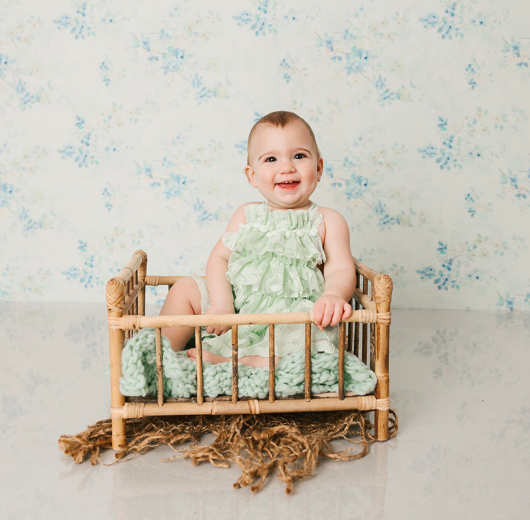 A happy toddler girl in a green dress sits in a wicker bed in a studio before visiting preschools erie pa