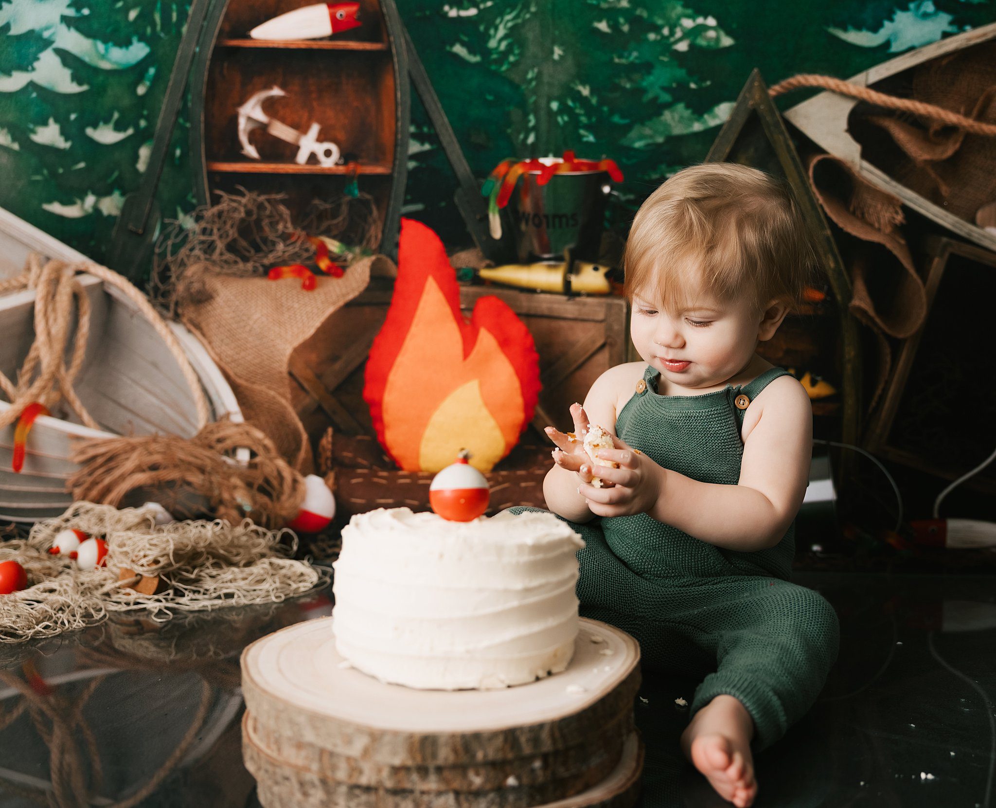 A young toddler boy in green knit overalls smashes a cake in a camping themed studio before summer camps erie pa
