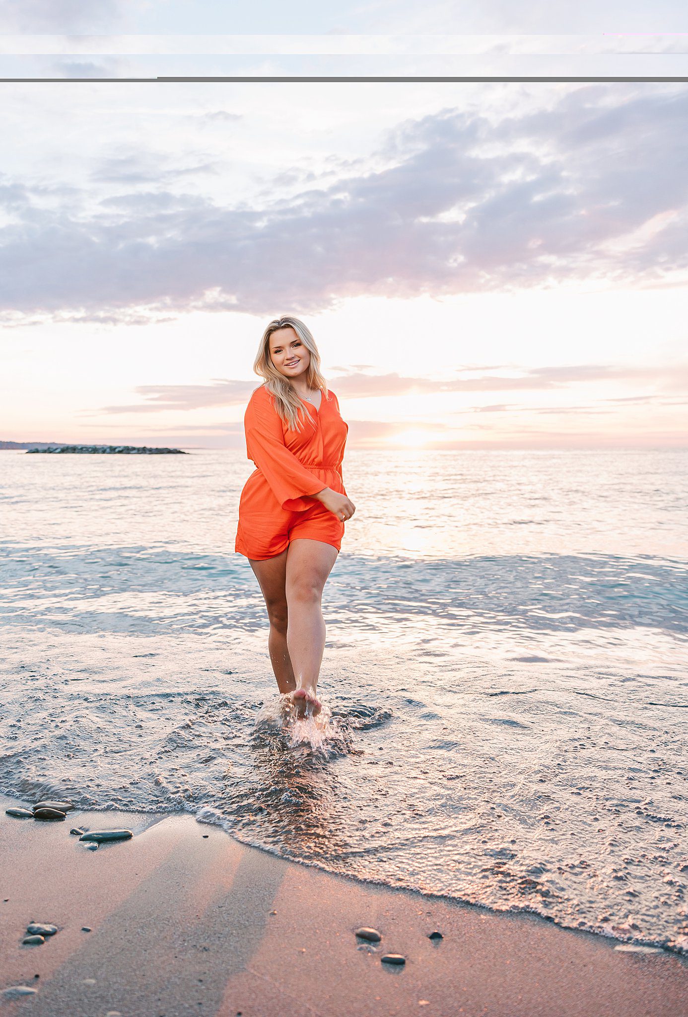 A woman in an orange romper plays in the water on the beach after visiting tanning salons in Erie, PA