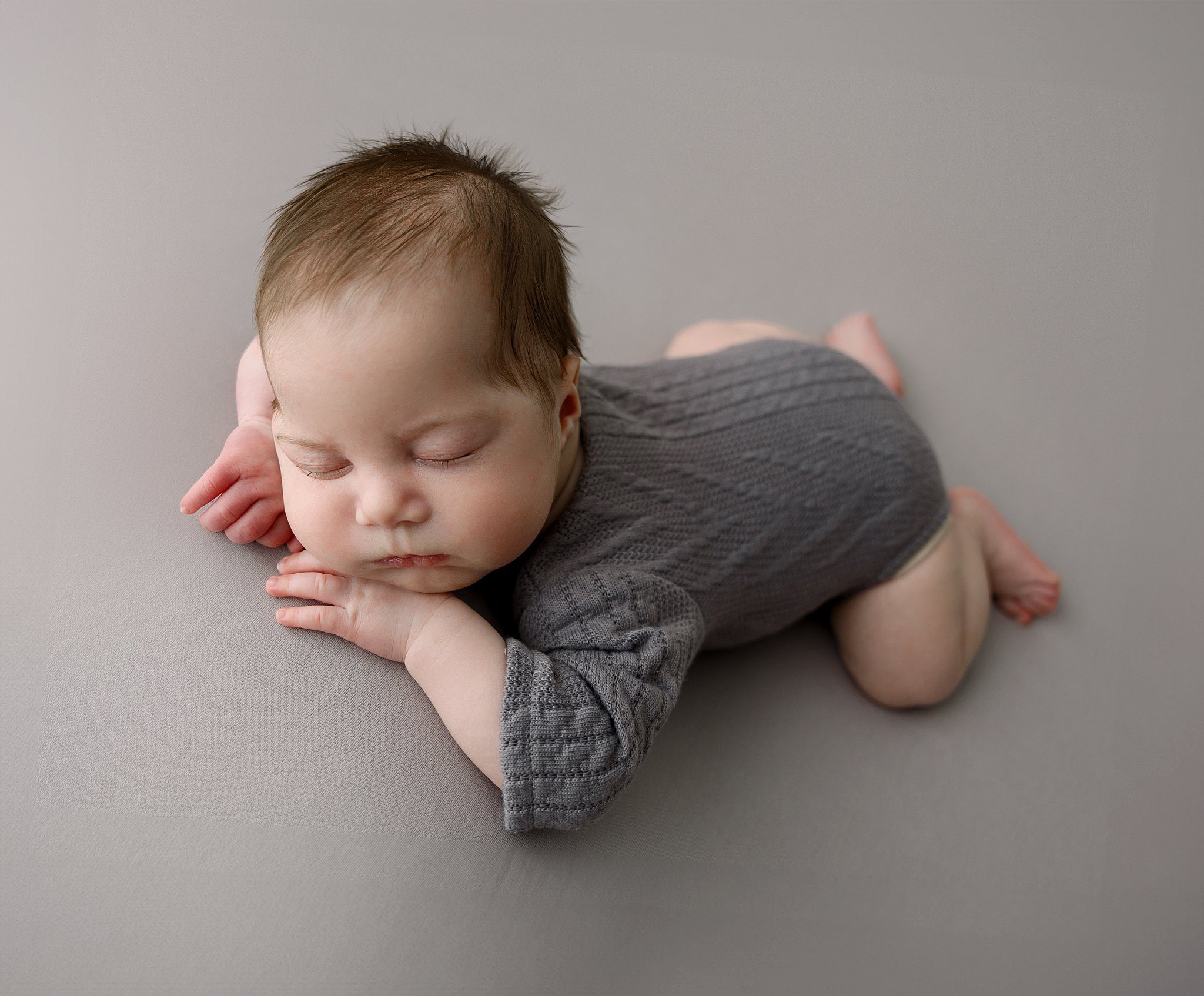 A newborn baby sleeps in a knit onesie on its tummy in a studio after mom had some upmc pelvic floor therapy